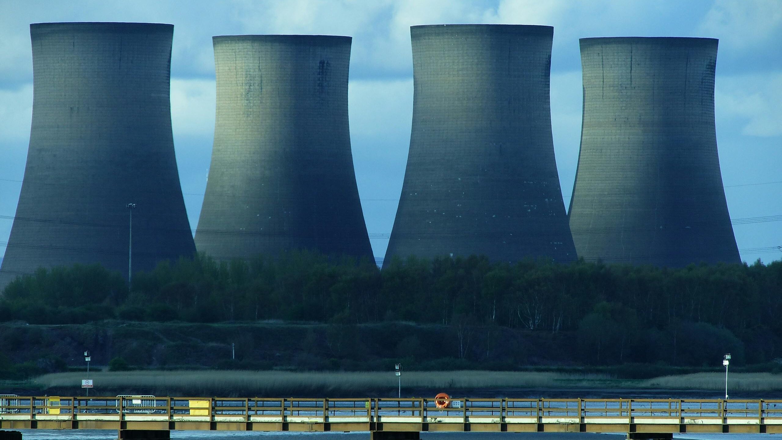 View of industrial cooling towers and a bridge over water, showcasing energy infrastructure.