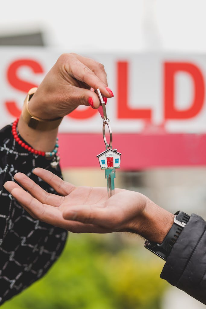 Foreign Asset Reporting Requirements:Close-up of hands exchanging house key with colorful SOLD sign in the background.