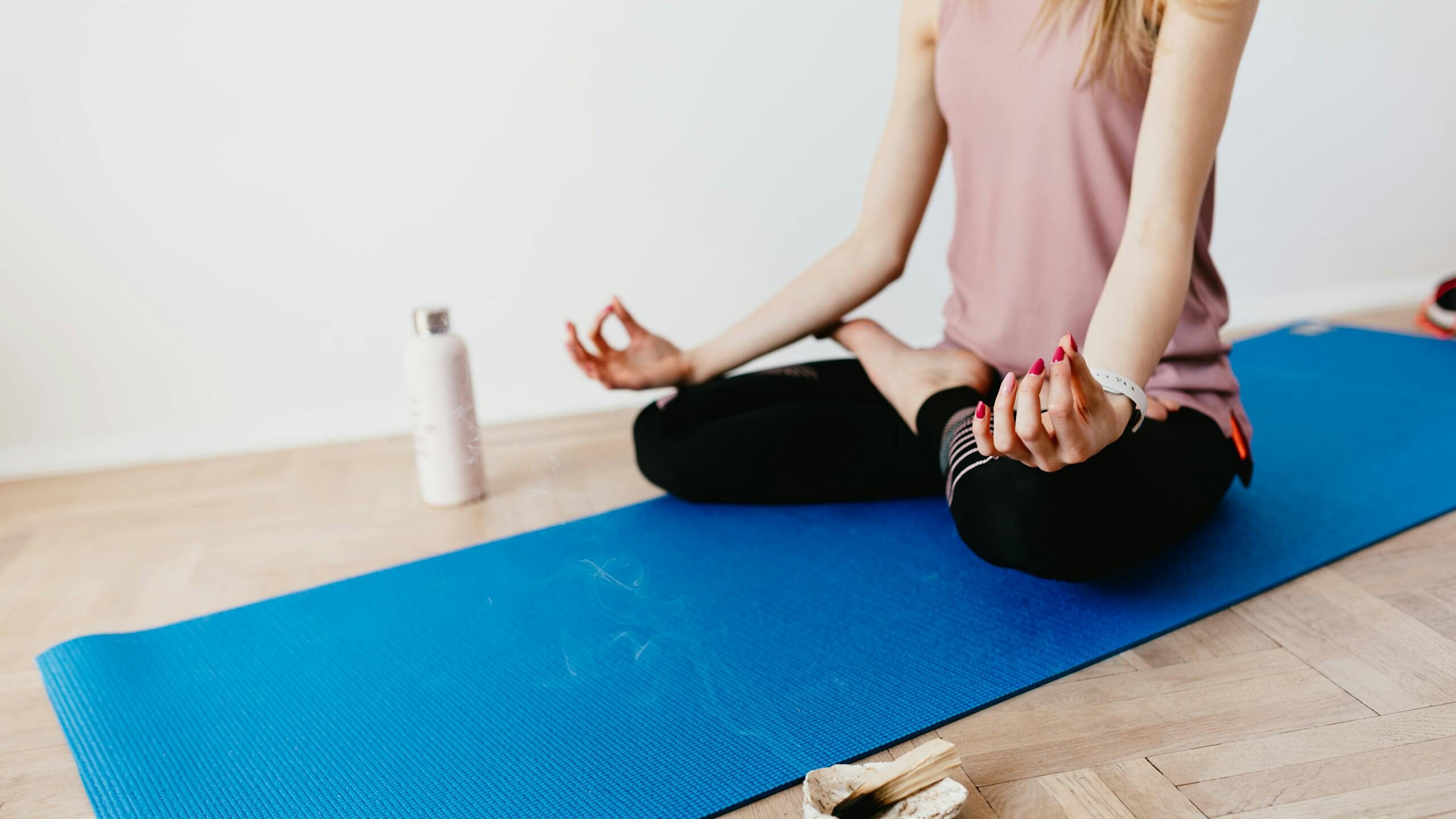 Young woman practicing yoga and mindfulness indoors on a blue mat with incense.